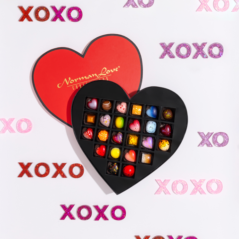 24 beautifully crafted chocolates in a red, heart-shaped gift box. The gift box includes 10 limited -edition hearts as well as 14 signature pieces. Pink, red, and purple XOXO surround the open gift box.